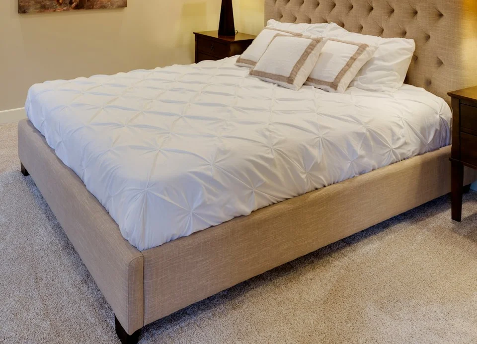 Beige upholstered bed base with visible fabric side and foot panels