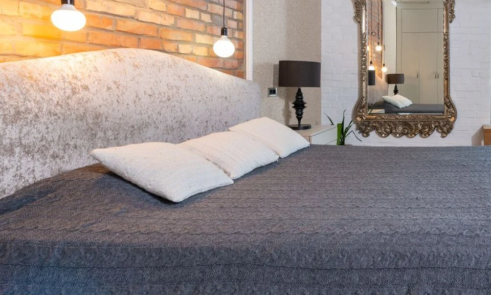 A cream patterned fabric headboard behind pillows in a naturally lit bedroom