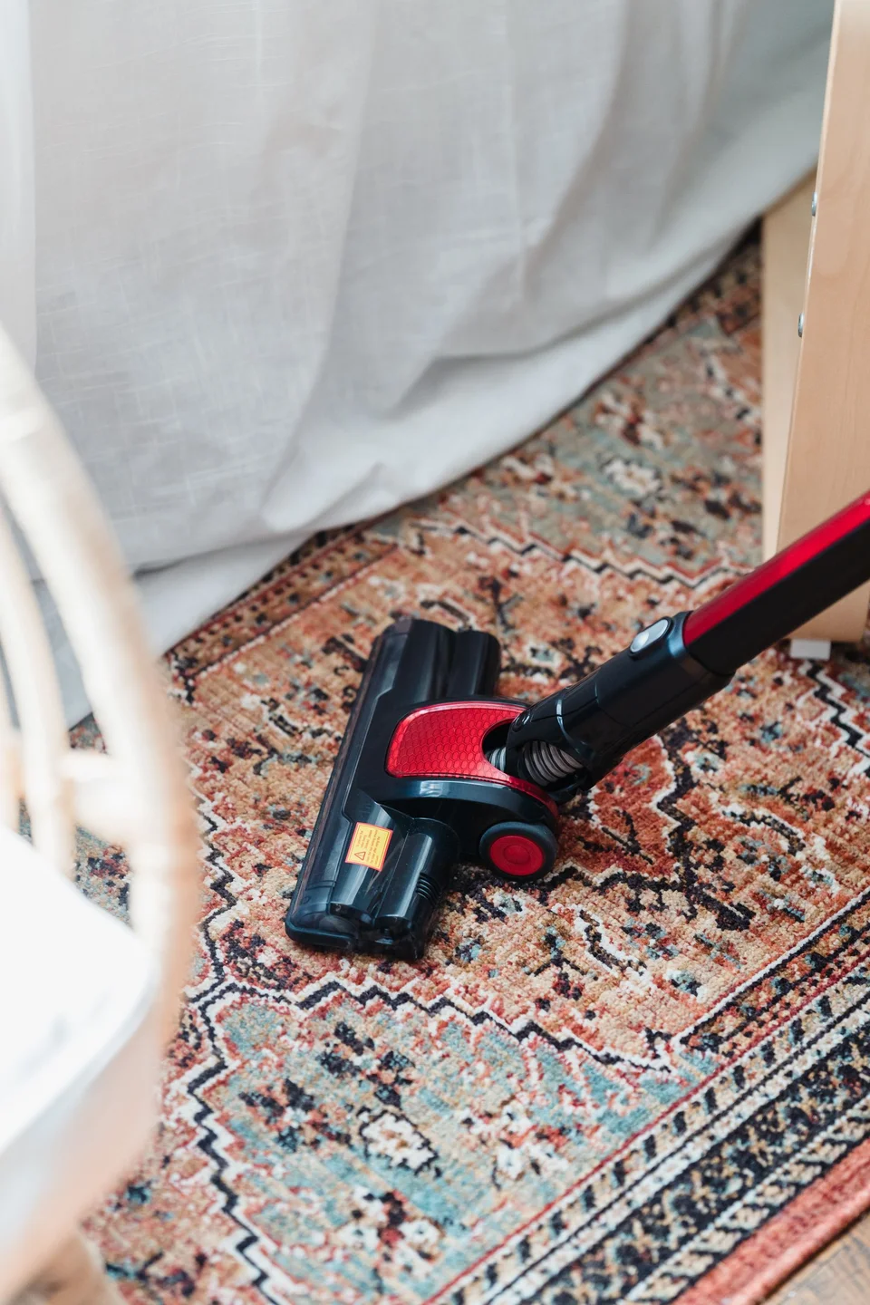A vacuum head cleaning a patterned loose rug on a wooden floor