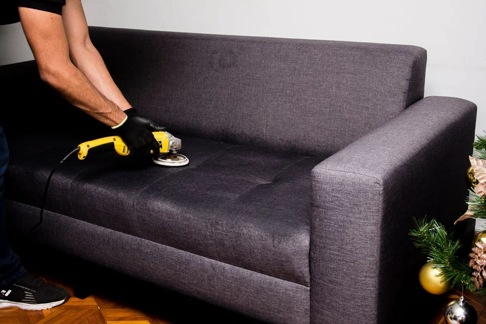 A cleaner using a rotary upholstery brush on a grey fabric couch